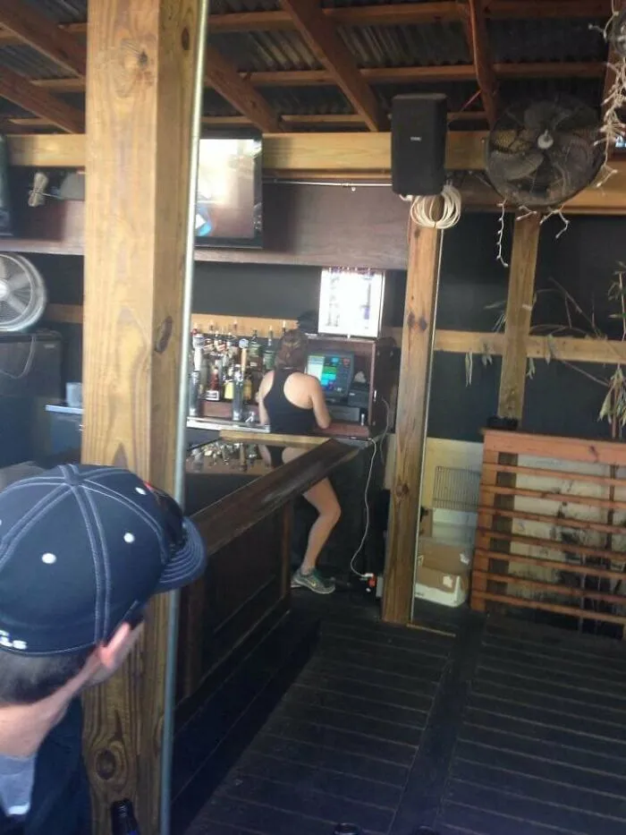 Amusing mirror pic where bar counter reflection creates optical illusion of a bartender in a swimsuit.