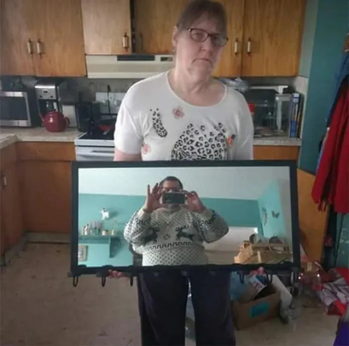 Woman holding a mirror with a man taking a photo seen in the reflection