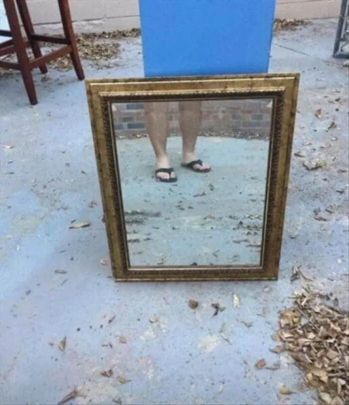 Bare legs and feet wearing flip flops visible in a framed mirror pic resting on the ground outdoors.