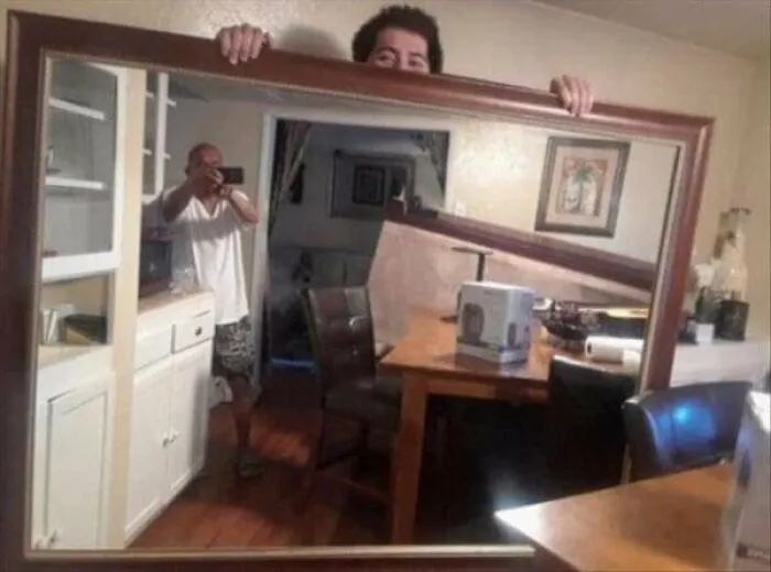 Funny mirror pics showing a man peeking over a framed mirror while taking a selfie reflection indoors