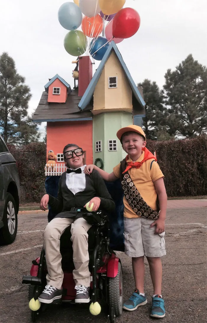 Two kids in movie Up costume, showcasing creative people with disabilities on Halloween with a house wheelchair.