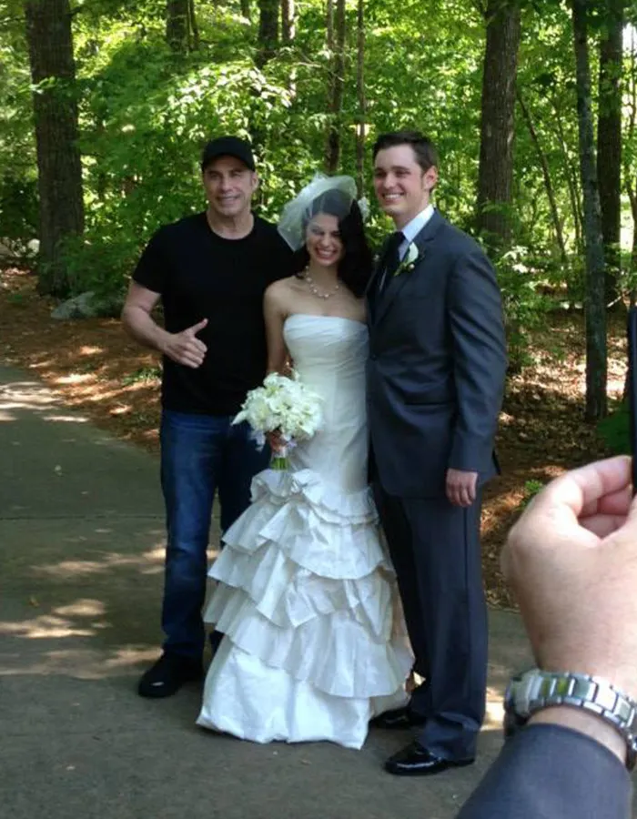 John Travolta posing casually with a bride and groom as surprise wedding guests.