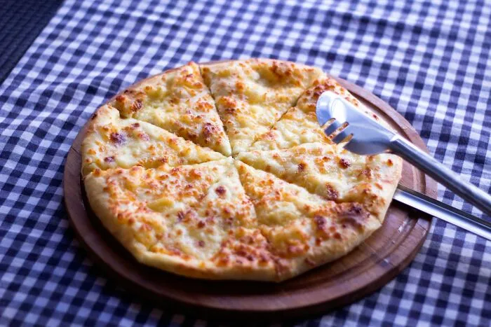 A freshly baked cheese pizza on a wooden board, relatable to worst MIL stories.