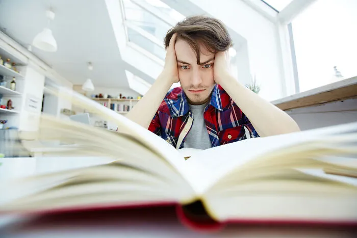 Frustrated young man with his head in his hands studying a book, illustrating health problems in Gen Z.