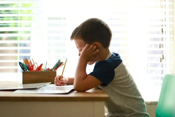 Frustrated young student writing with a pencil, feeling the pressure from infuriating teachers.
