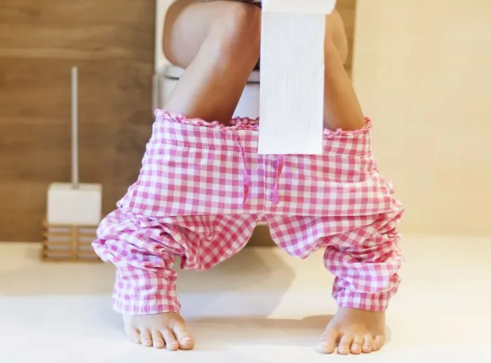 A person using the toilet with pink checkered pajamas down. Everyday health things women wish they knew.