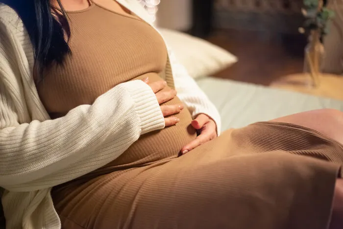 A pregnant woman in a beige dress holding her belly, representing people disowned by their families.