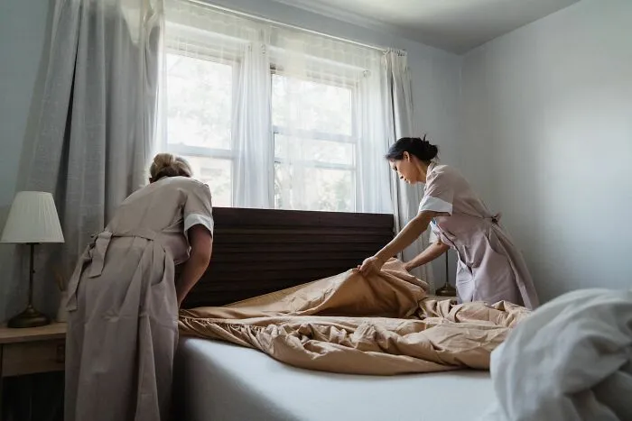Two housekeepers making a bed in a rental room related to Airbnb stories