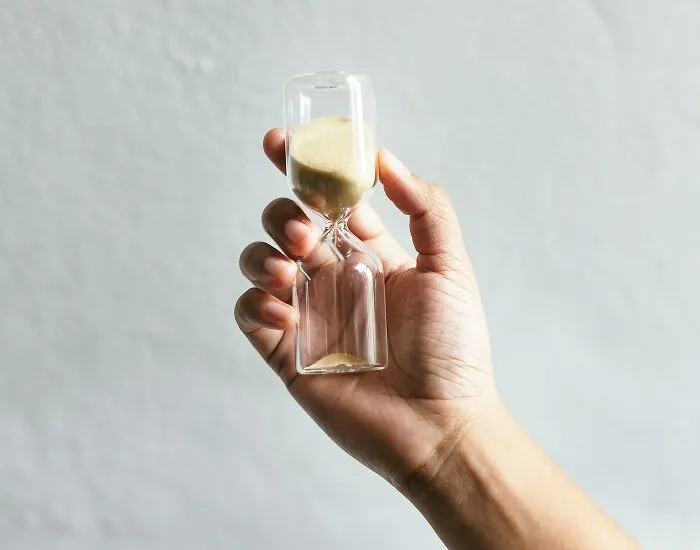 A hand holding a small glass hourglass, representing time in wild Airbnb stories.