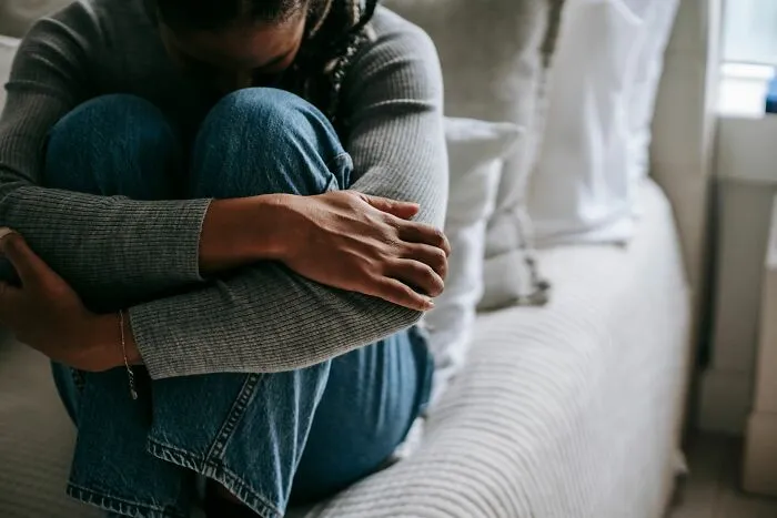 A stressed woman sitting on a bed hugging her knees, illustrating difficult Airbnb stories.