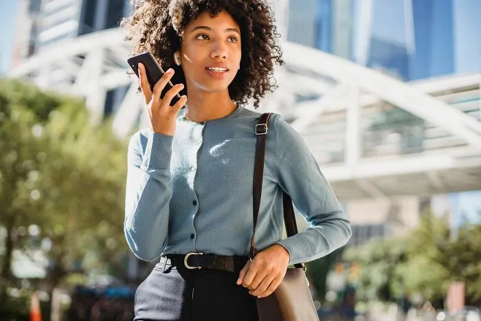 A woman holding a smartphone and listening to a voice message outdoors, dealing with Airbnb Host tasks.