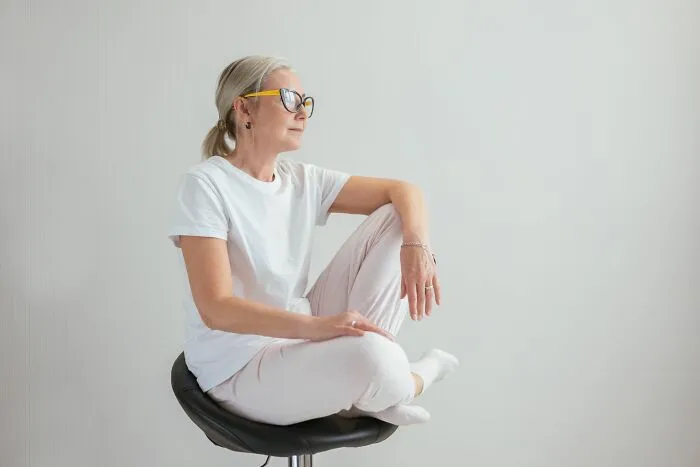 An Airbnb Host sitting cross-legged on a chair, thoughtfully looking off to the side.