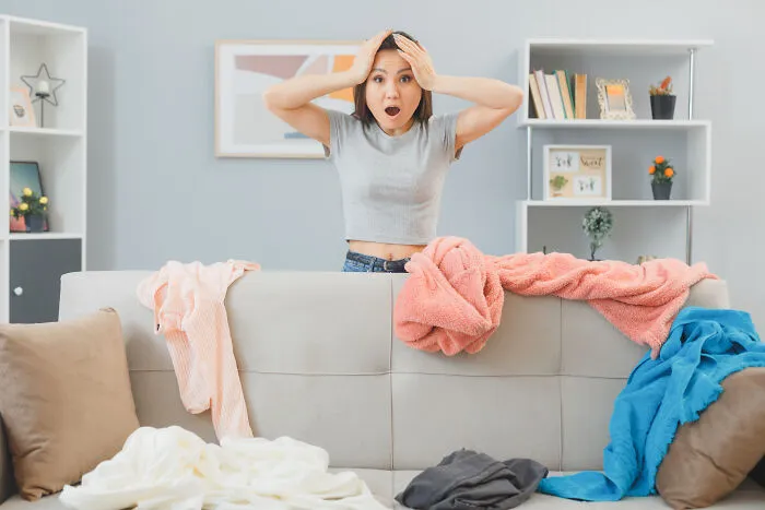 A shocked woman holding her head over a messy sofa in a room, illustrating crazy Airbnb stories.