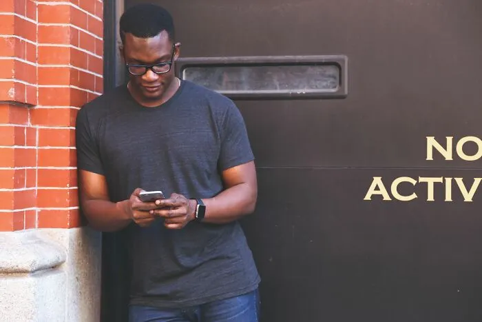 A young man in glasses texting on his smartphone outside a building, related to host Airbnb stories.