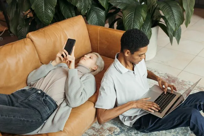 A man using a laptop and a woman on a couch looking at her phone, representing Airbnb stories.