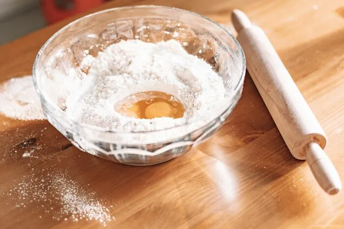 A glass bowl with flour and an egg next to a rolling pin on a table, illustrating Airbnb host experiences.