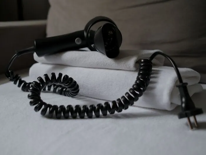 A black hair dryer on folded towels creates spooky things vibes with its eerie coiled wire.