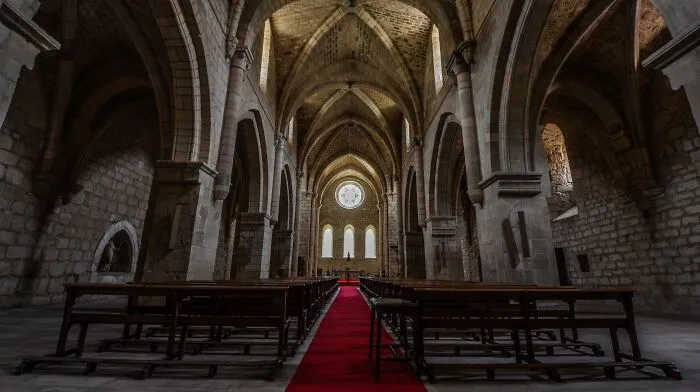 The dark interior of an ancient stone cathedral with spooky vaulted ceilings and empty pews