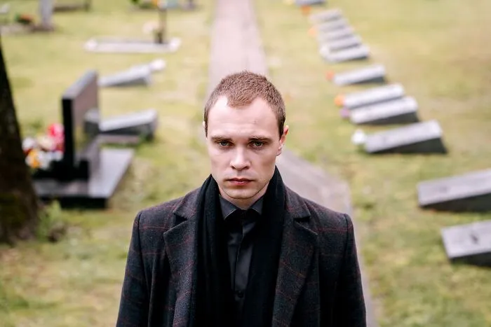A man wearing a black coat standing in a graveyard, recalling spooky things in cemetery settings.