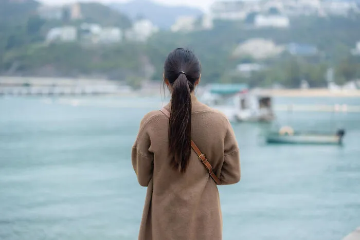 Woman in brown coat looking at misty waterfront creepy stories