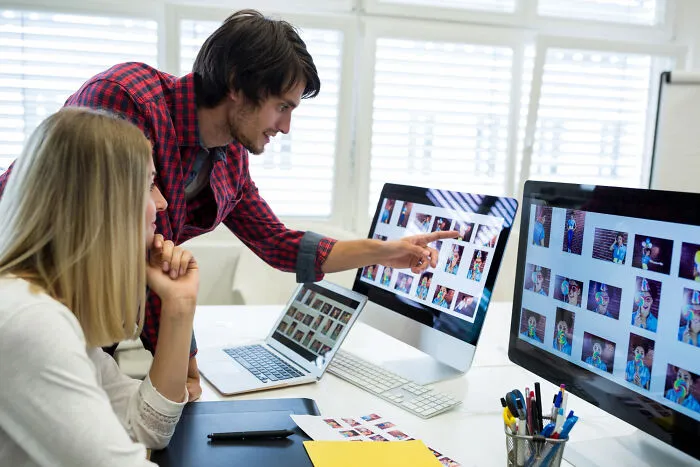 Colleagues selecting photos on computer screens in office
