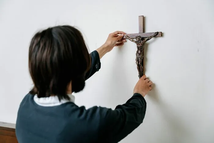 Person hanging crucifix on white wall indoors