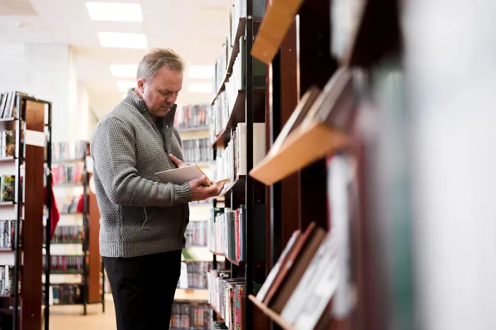 Middle-aged man selecting a book from library shelves