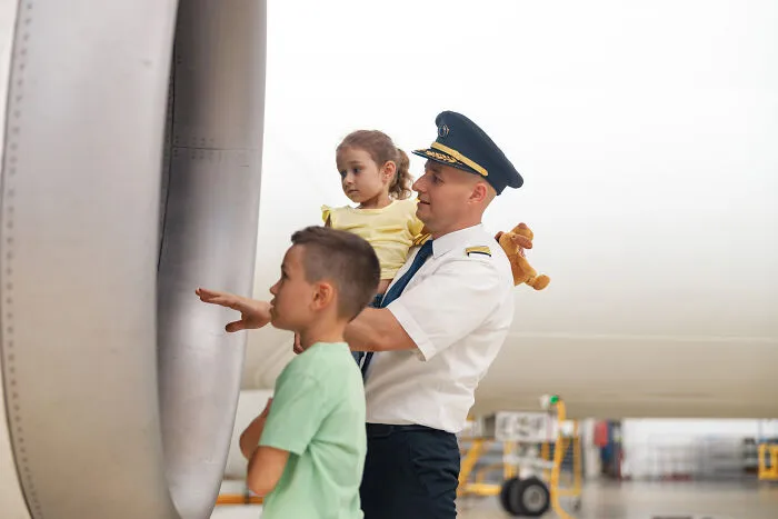 Pilot holding a young girl and showing airplane engine to a boy