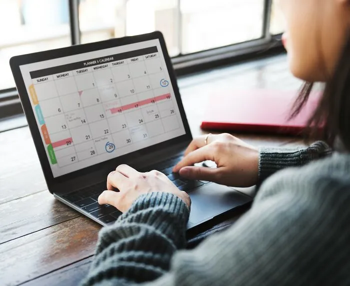 A person typing on a laptop looking at a calendar, planning around worst MIL stories.