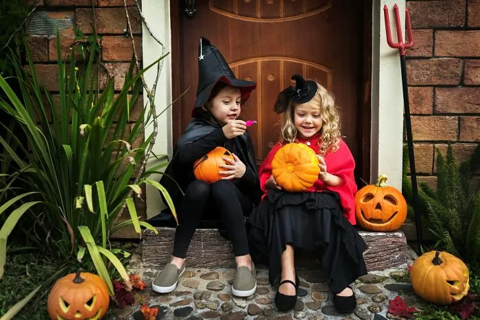 Two young girls in Halloween witch costumes sitting on porch steps holding carved pumpkins