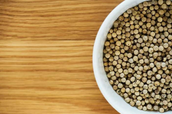 White peppercorns in a ceramic bowl on a wooden surface, showing brilliant tips for cooking.