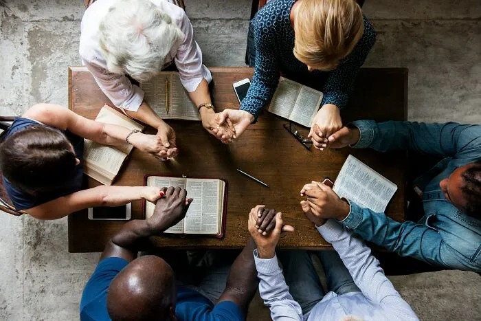 Group sitting around a table holding hands, showcasing industry insiders gathered together.