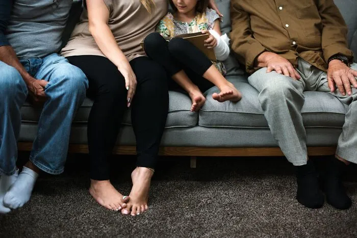 Family members sitting together on a grey couch indoors.