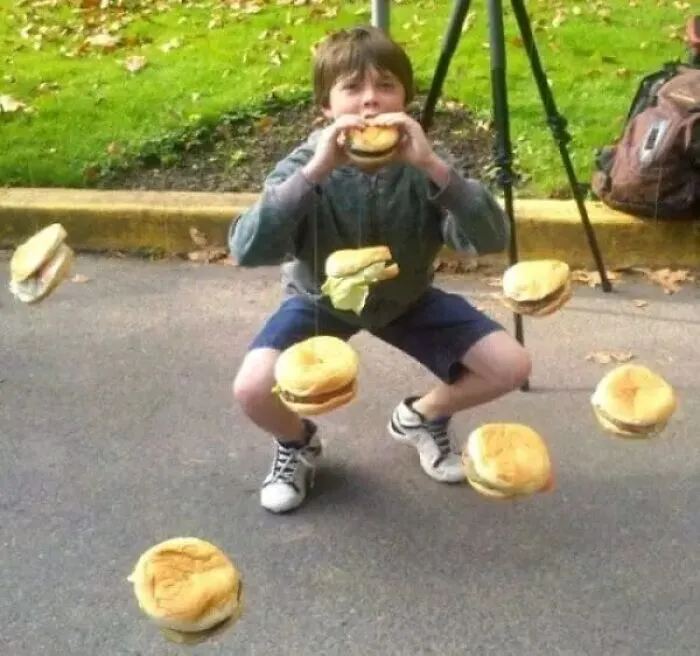 Boy squatting outdoors surrounded by floating hamburgers weird cursed image