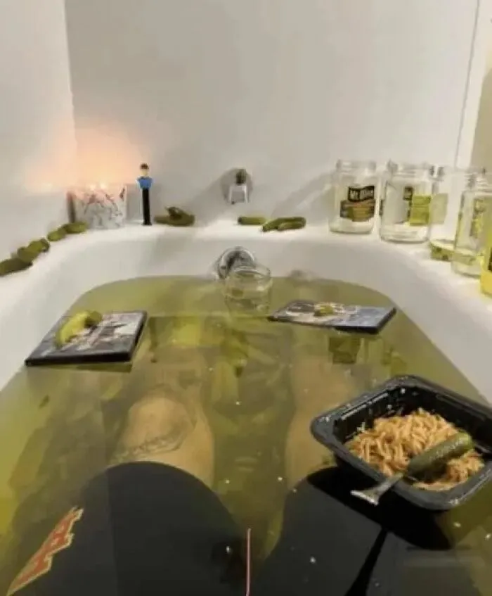 Cursed image of person bathing in murky water with pickles and jars around.