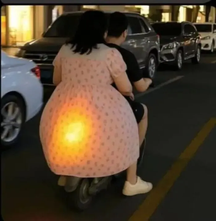 Cursed image of person on scooter with illuminated dress creating glowing effect.