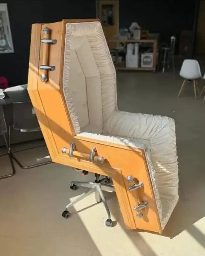 Office chair shaped like a coffin with padded interior and metal handles