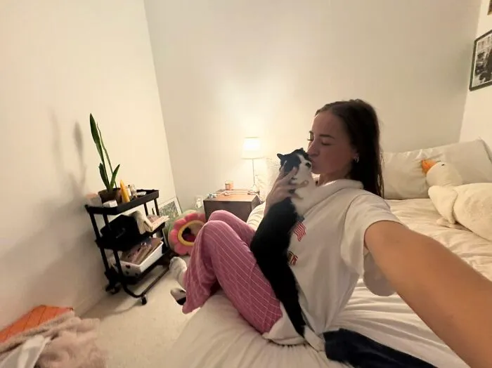 Woman kissing her black and white cat on bed in viral TikTok trend of life stories lived alongside pets