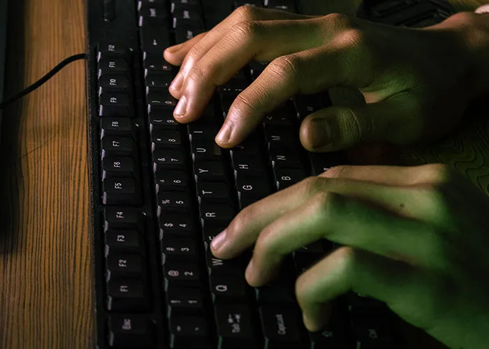 Close-up of hands typing fast on a dark computer keyboard to investigate strange online mysteries.
