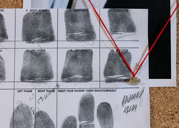 Fingerprint card pinned with red string on an investigation board tied to online mysteries.