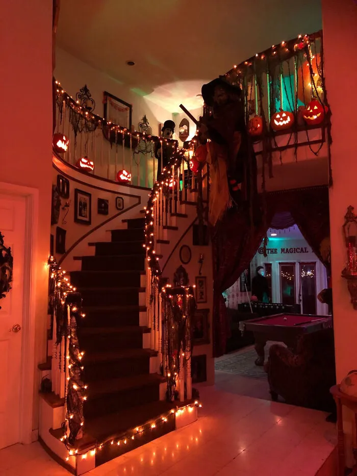 Grand staircase wrapped in warm orange fairy lights and jack-o-lanterns as Halloween house decoration.