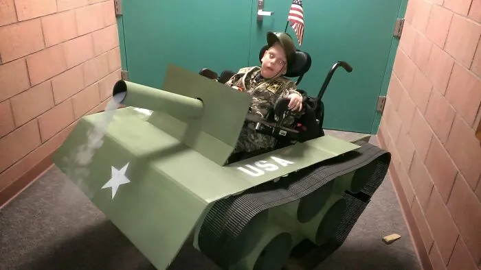 A child in a military costume using an army tank wheelchair cover for a hilarious Halloween outfit idea.
