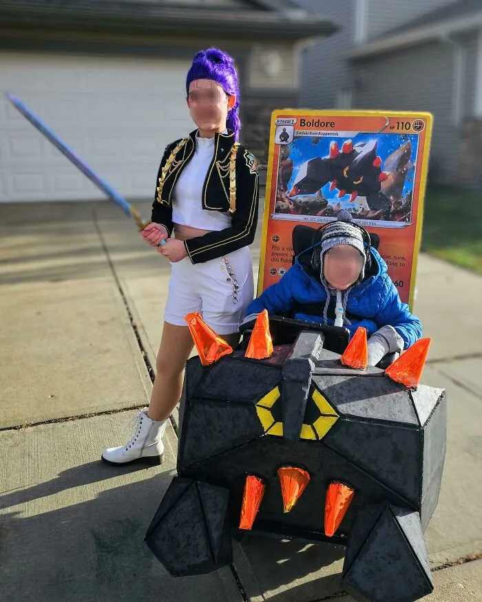 A child in a Pokemon Boldore wheelchair costume posing alongside a cosplayer for a fun Halloween look.