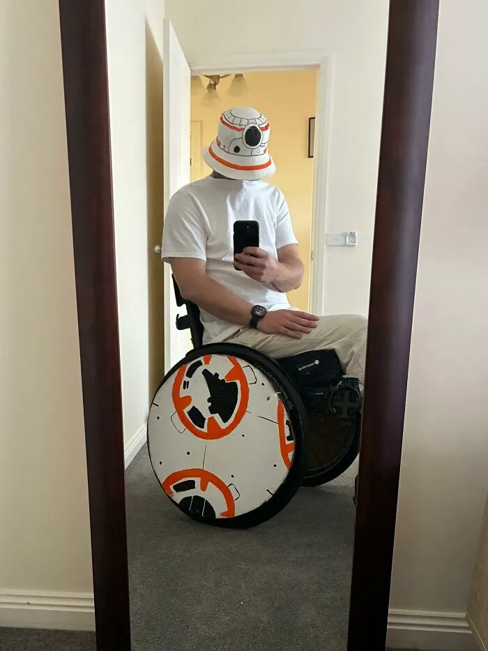 A man in a wheelchair with Star Wars BB-8 custom wheel covers showing creative Halloween costumes for disabled people.