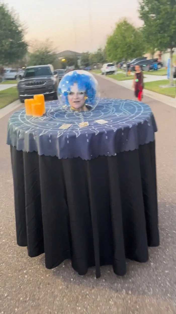 Woman sitting inside a fortune teller table costume made for creative people with disabilities on Halloween.
