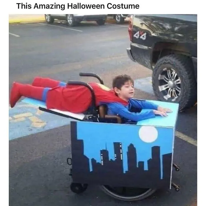 A young boy in a wheelchair disguised as Superman flying over a city for Halloween