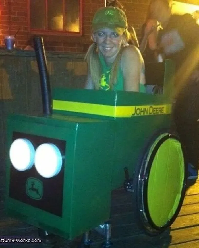 A woman smiling in a wheelchair customized into a green John Deere tractor for Halloween.