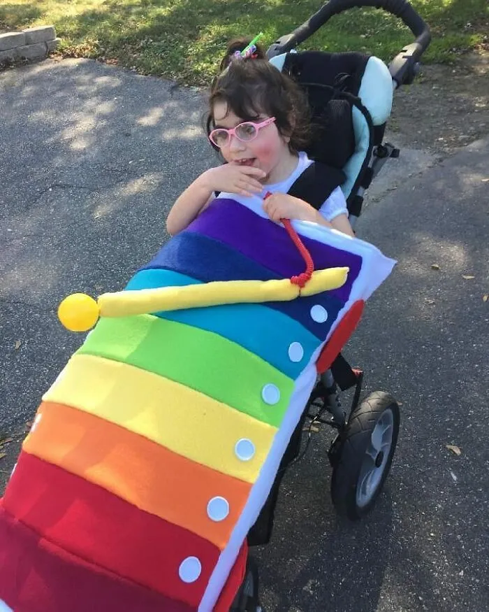 A young girl in a stroller dressed as a colorful xylophone for a creative Halloween costume.
