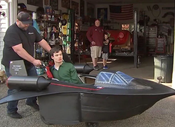 Man pushing a teenager in an elaborate Batmobile wheelchair costume as part of people with disabilities Halloween ideas