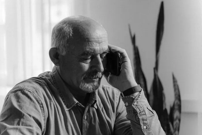 Elderly man speaking on phone appearing reflective in black and white patient communication